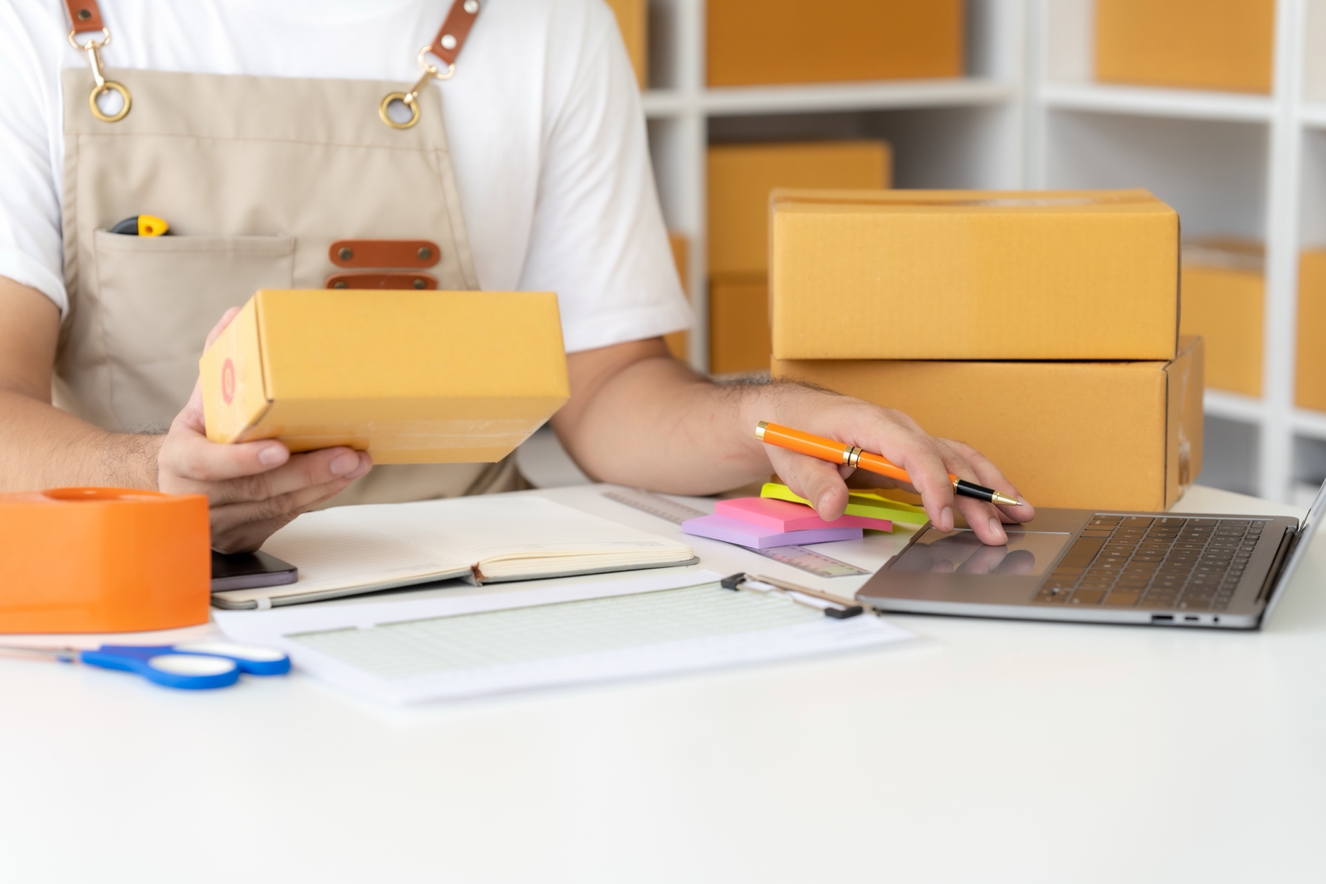 Small business owner working through manual packing and paperwork at a cluttered desk