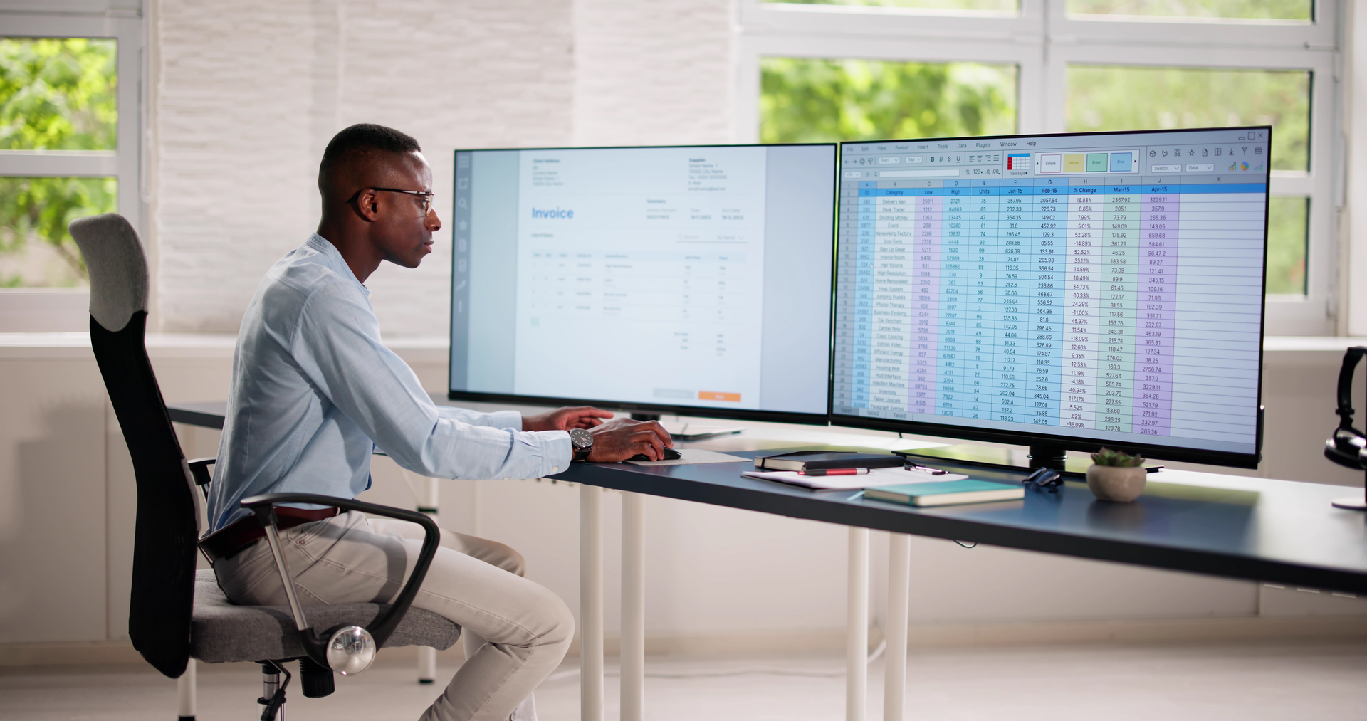 Business owner copying figures between an invoice and a spreadsheet on two monitors